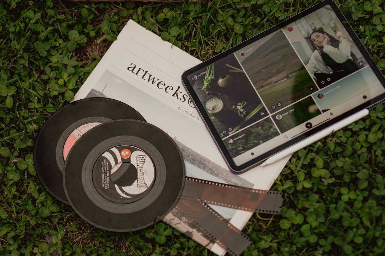 A flat lay of vintage films, a newspaper, and a tablet on grass.